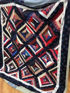A partially-finished quilt with diamonds made of string piecing in red white and blue with patriotic fabrics as well 