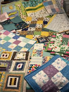 A collection of baby quilts in blues, greens, yellows and golds, tossed in a very cozy pile 