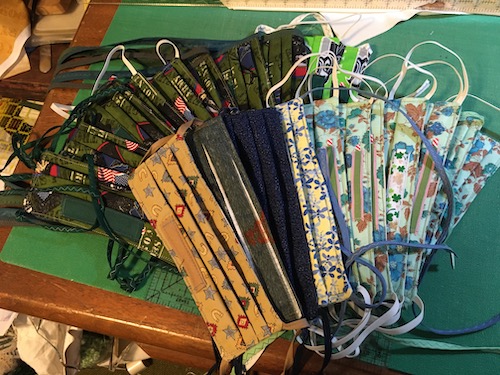 A table of handmade pleated face masks with ear elastic in a variety of prints and colors 