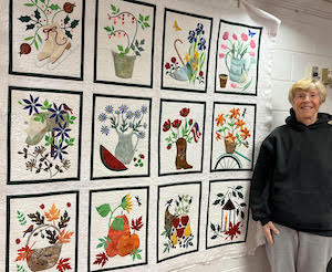Bunny Tjaden standing next to an applique quilt of the 12 months, eah with a design that incorporates flowers and seasonal colors