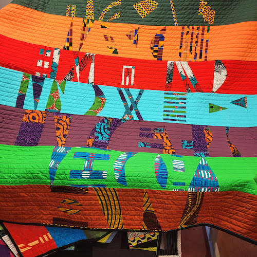 An abstract, modern quilt in oranges, reds and greens with African print fabric designed by Eleanor Balaban.